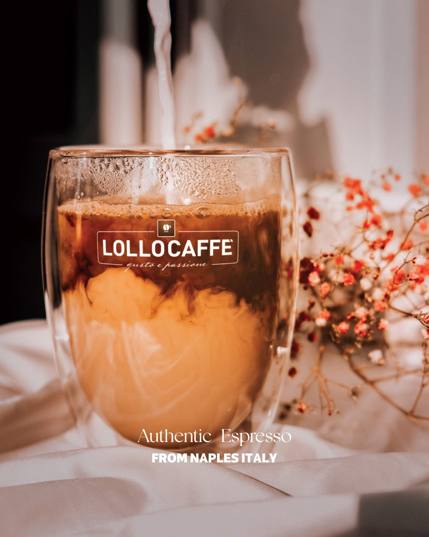 Bicchiere di caffè freddo con espresso e latte, vicino a un piccolo mazzo di fiori. Logo 