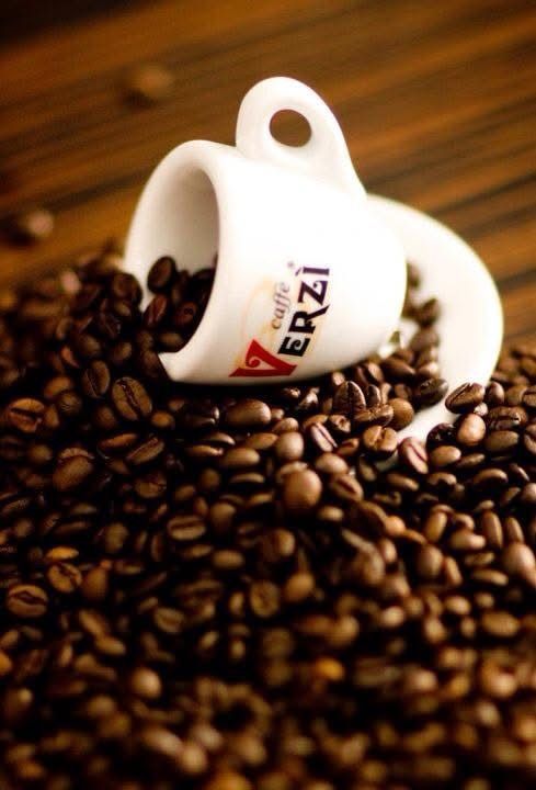 Tazza da caffè bianca rovesciata che rovescia chicchi di caffè tostati su un mucchio di chicchi, su una superficie di legno.