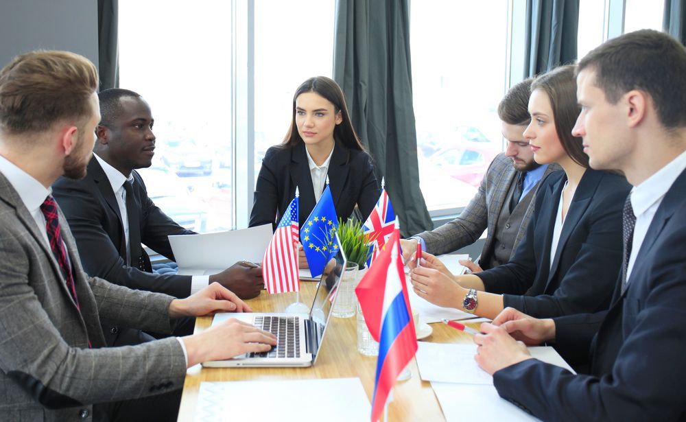 Un grupo de empresarios, sentados a una mesa con banderas de Estados Unidos, la Unión Europea, Reino Unido y Rusia, participaban en una conversación.