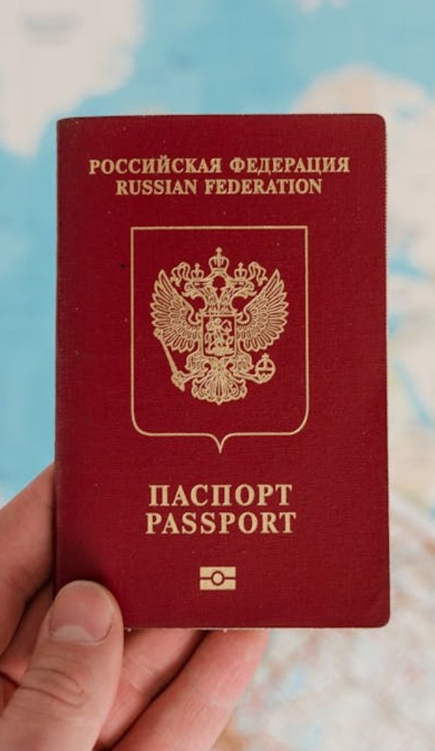 Pasaporte ruso rojo sostenido en la mano. El pasaporte tiene letras y emblema dorados.