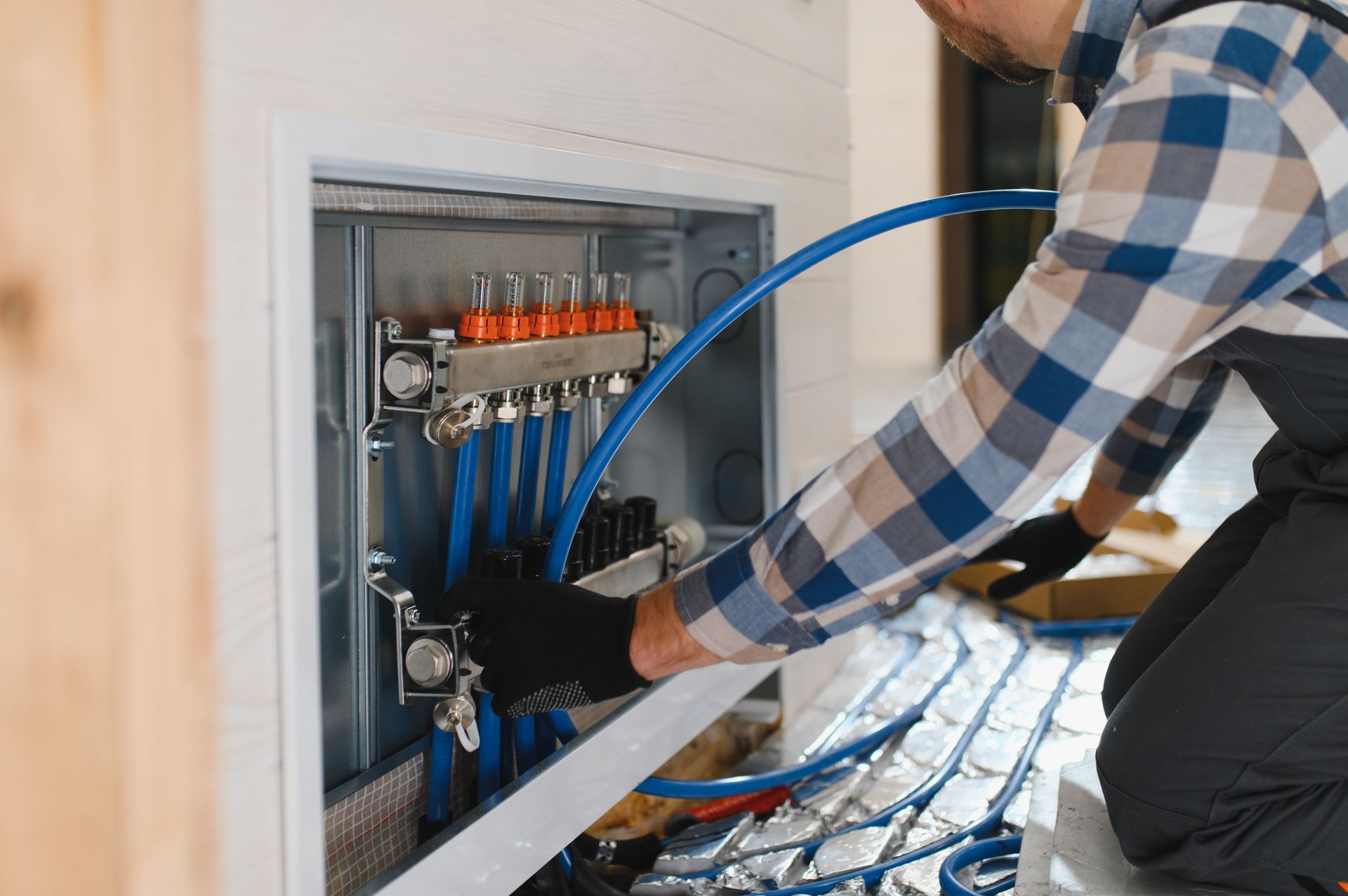 A person in a plaid shirt connecting blue pipes to a manifold in a white utility box. A person in a plaid shirt connecting blue pipes to a manifold in a white utility box.
