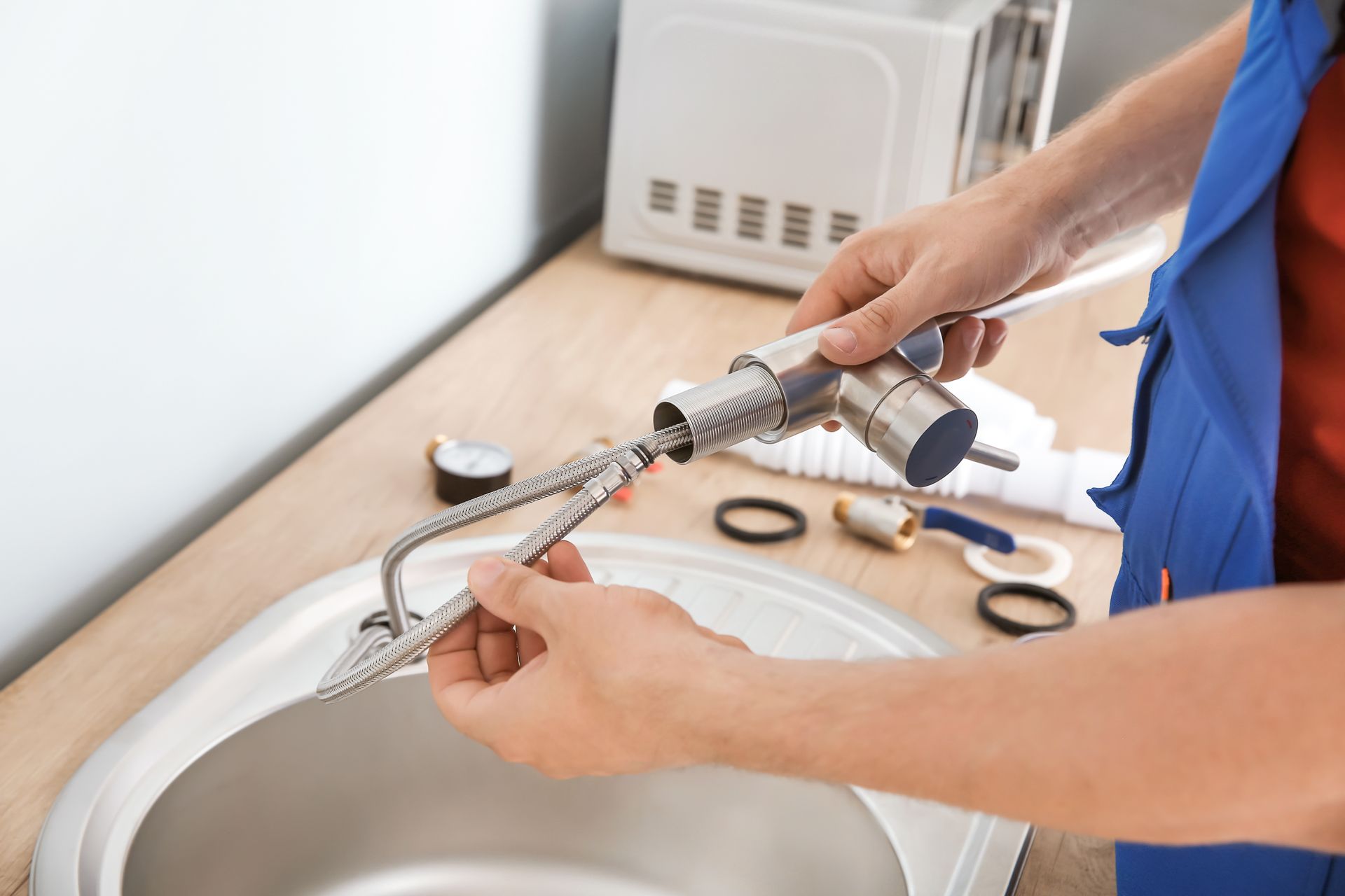 Plumber fixing kitchen sink; holding faucet with tools, parts, and sink visible. Plumber fixing kitchen sink; holding faucet with tools, parts, and sink visible.