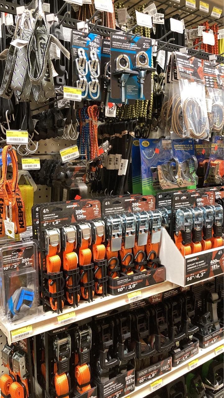 Shelves stocked with various hardware tools and tie-down straps in a store.