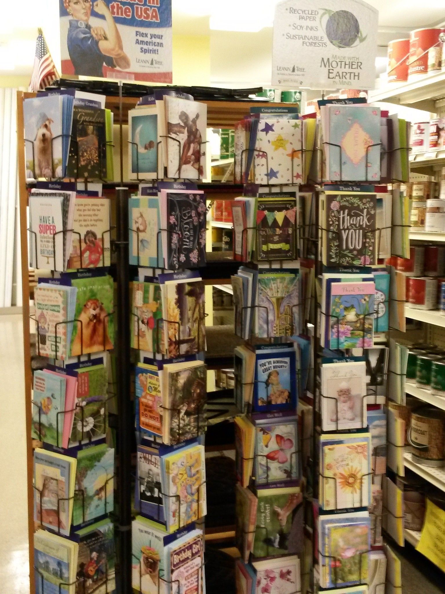 Greeting cards displayed on a rotating rack inside a store; shelf with canned goods is to the right.