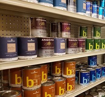 Shelves stocked with various paint cans, primarily Benjamin Moore brand, in a store setting.