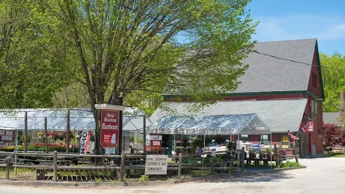 A red garden center building with greenhouses, sign, and wooden fence.