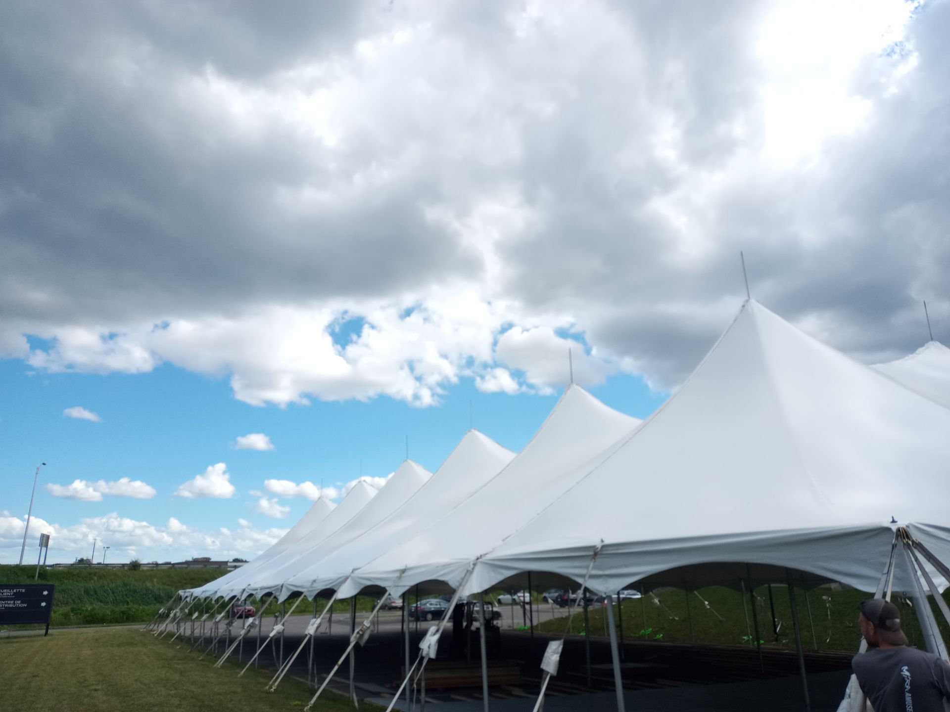 Une rangée de tentes blanches est alignée dans un champ par temps nuageux.