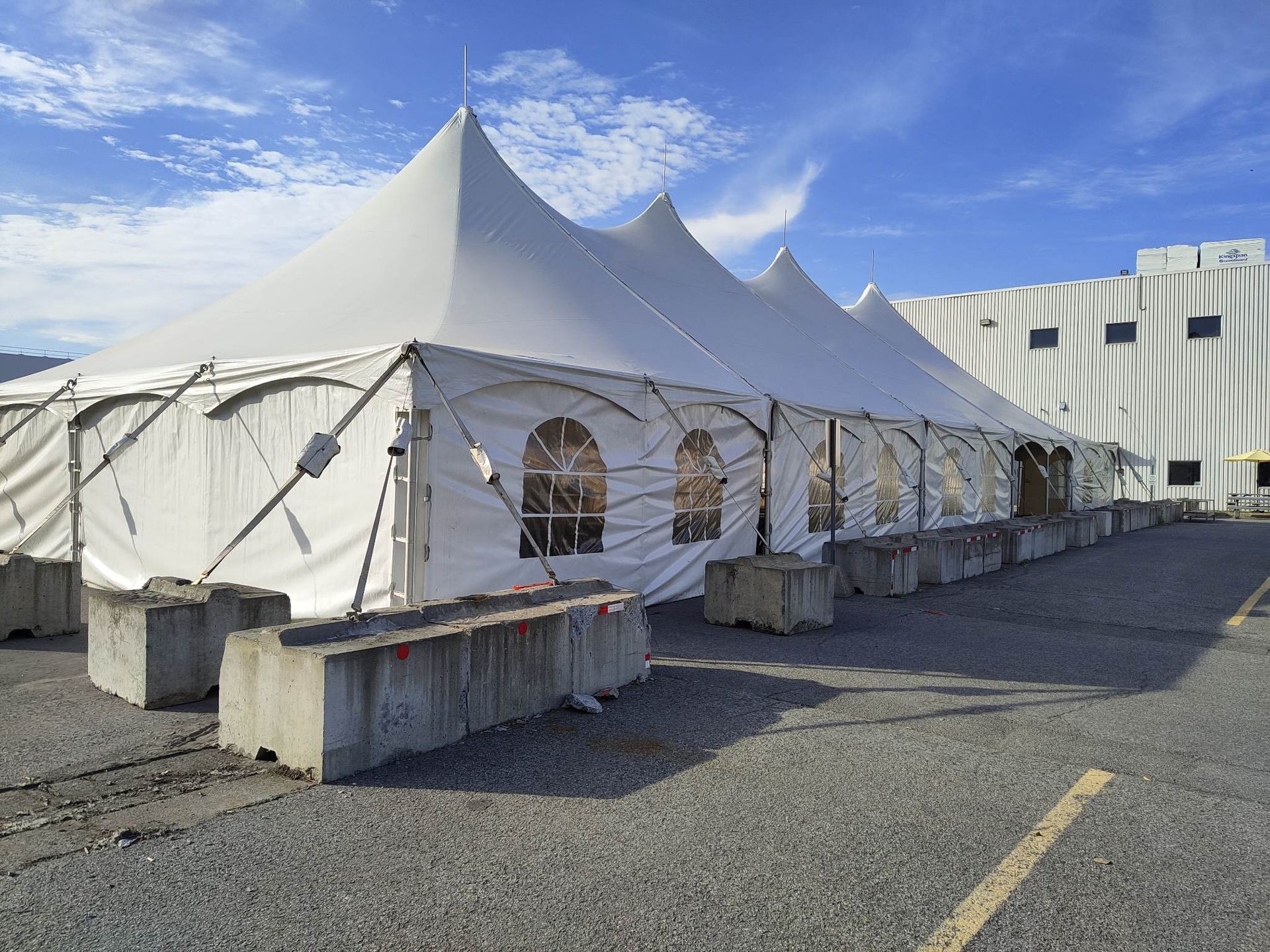 Une rangée de tentes est installée sur un parking devant un immeuble.