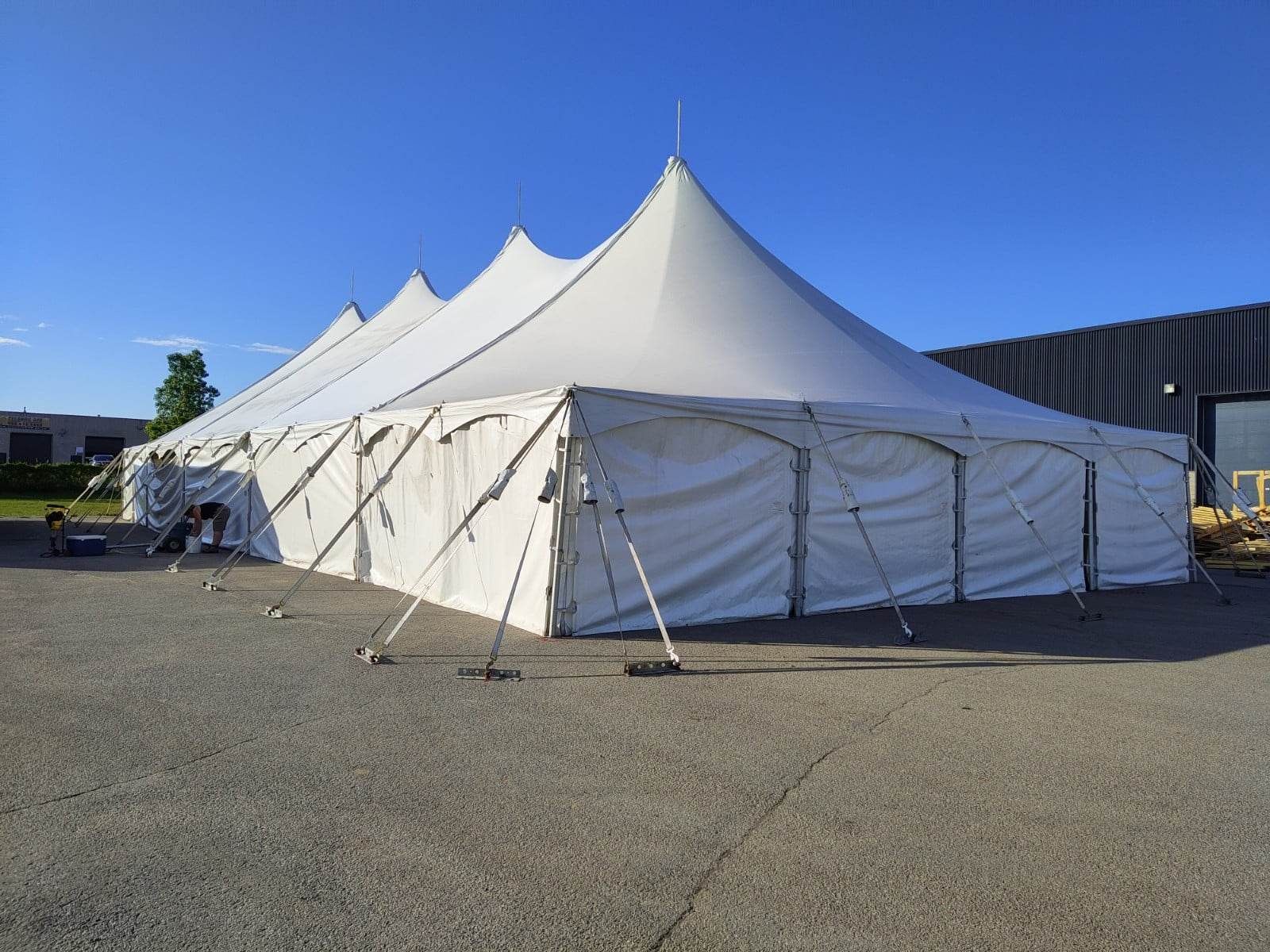 Une grande tente blanche trône au milieu d’un parking.