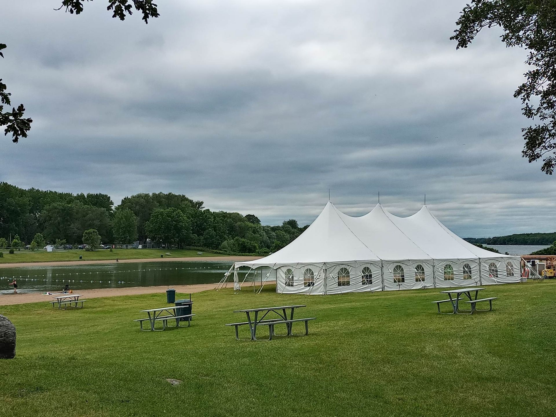 Une grande tente blanche est installée au milieu d’un champ herbeux à côté d’un lac.