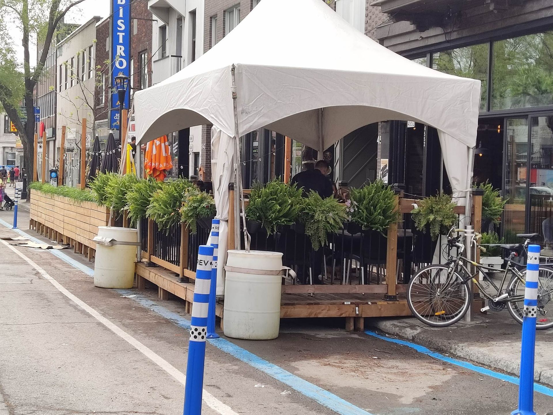 Une tente blanche est posée au bord d’une rue, à côté d’un panneau indiquant bistro
