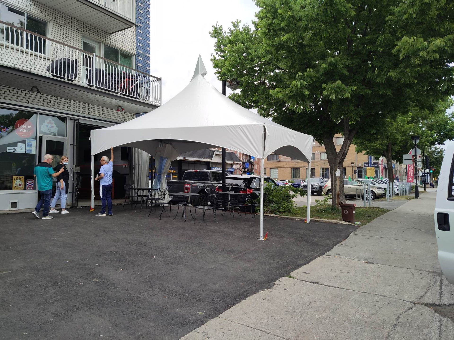 Une tente blanche est installée au bord de la route, devant un immeuble.