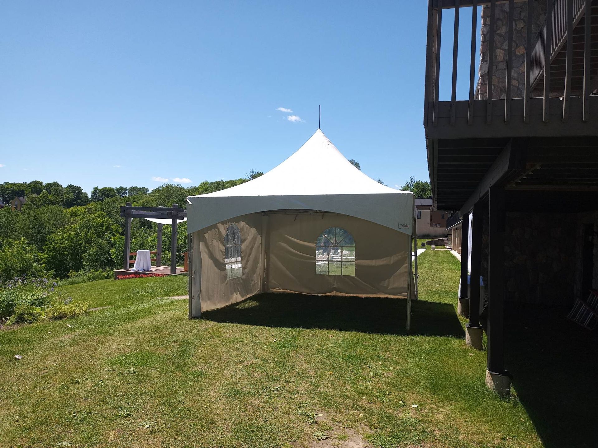 Une tente blanche est posée dans l’herbe devant une maison.