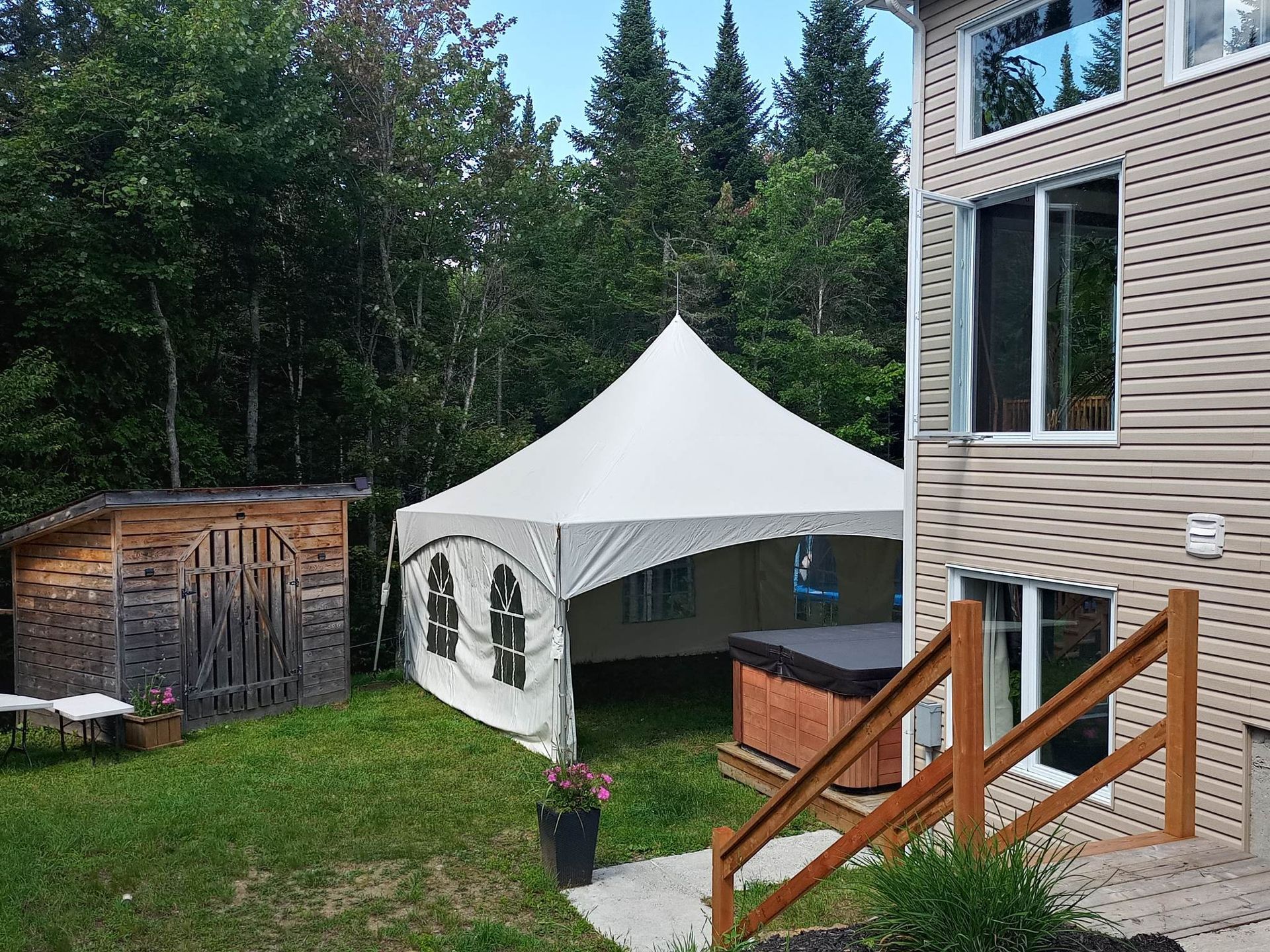 Une tente blanche est posée dans l’herbe devant une maison.