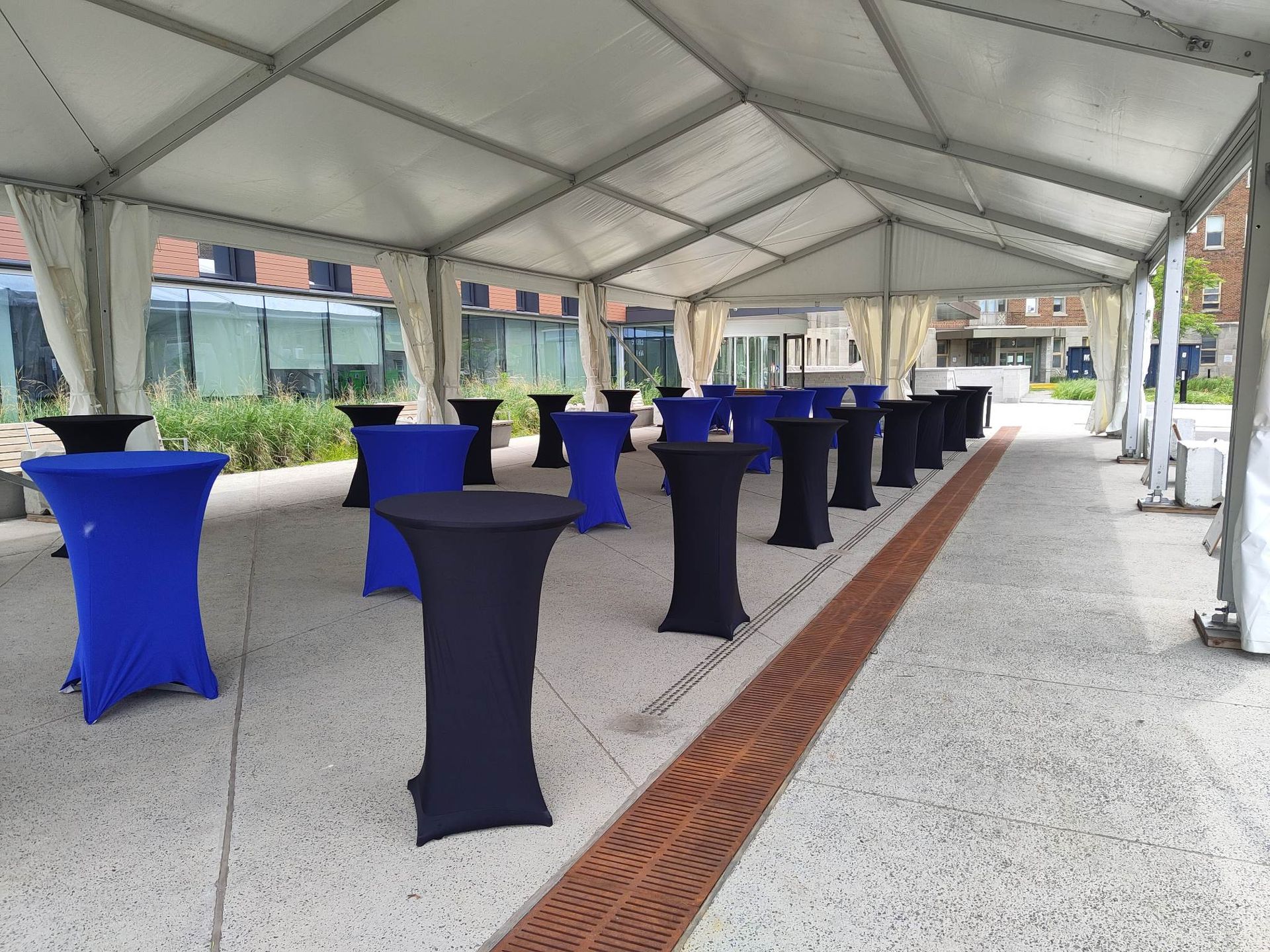 Une rangée de tables bleues et noires sous une tente.