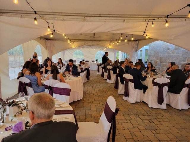 Un groupe de personnes sont assises à des tables sous une tente lors d’une réception de mariage.