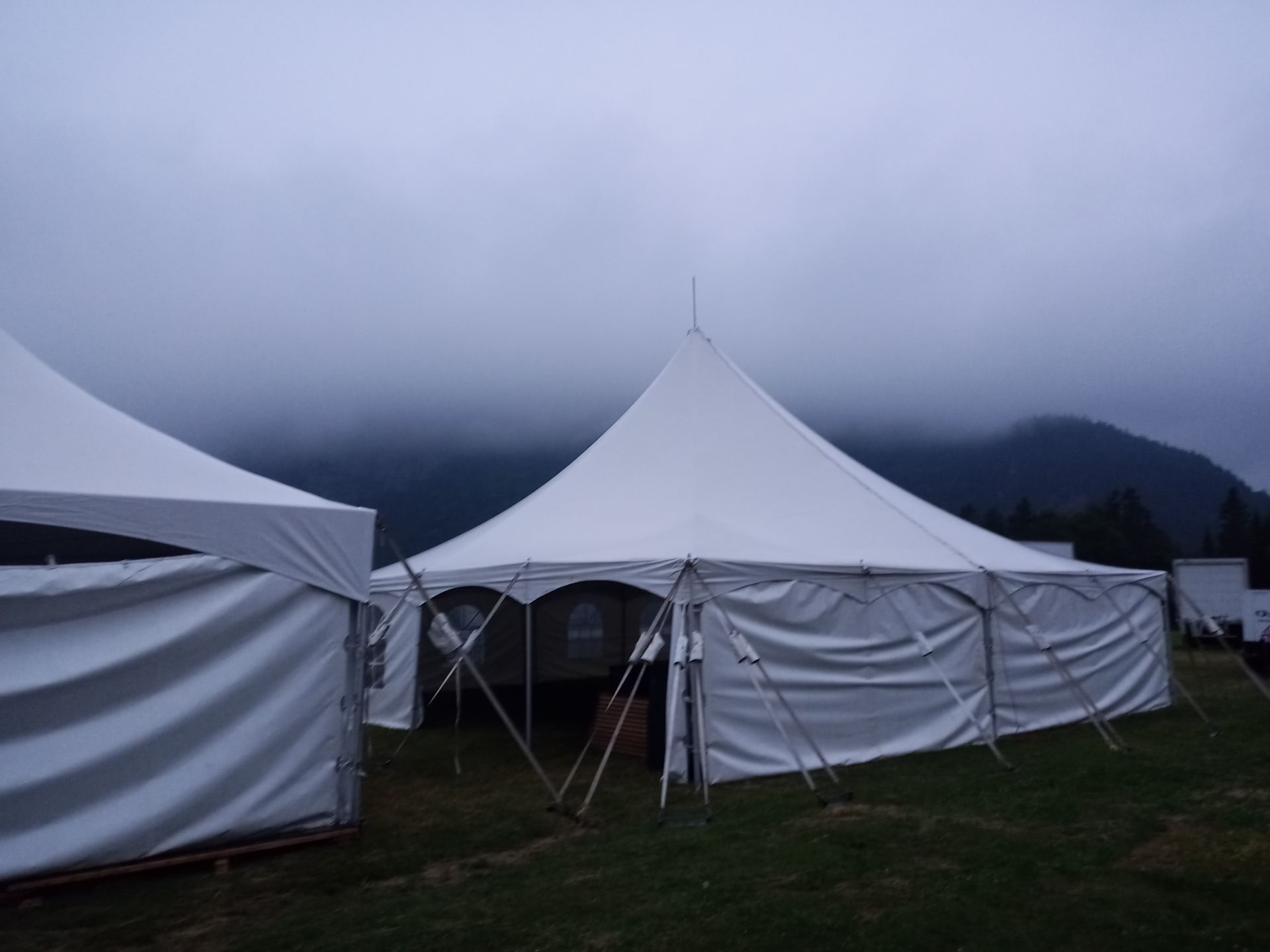 Une grande tente blanche dans un champ avec des montagnes en arrière-plan