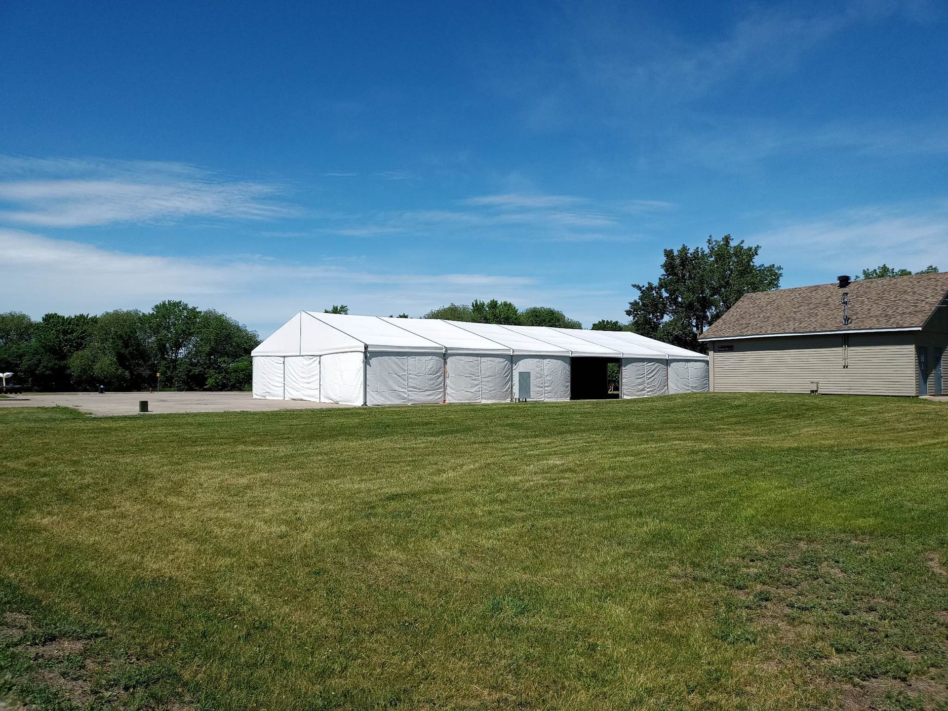 Une grande tente blanche est dressée au milieu d’un champ herbeux.
