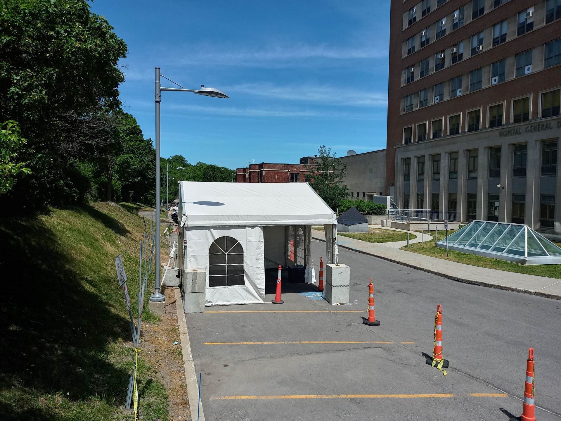 Une tente blanche est installée sur un parking à côté d’un immeuble.
