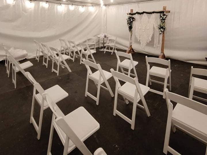 Une rangée de chaises pliantes blanches est alignée dans une tente.