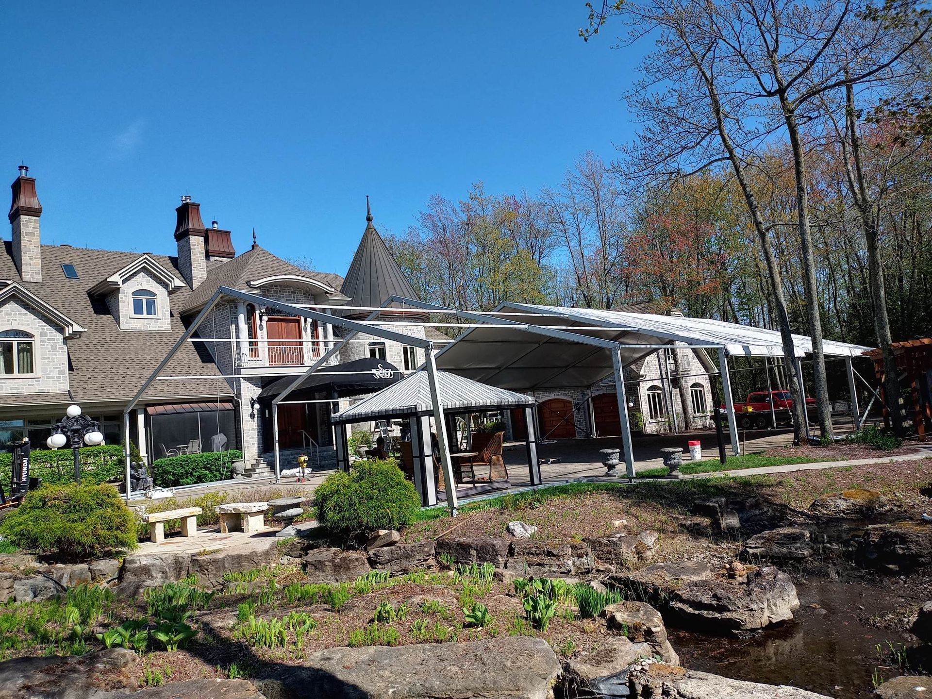 Une grande maison avec une grande tente devant elle est entourée d arbres et de rochers.