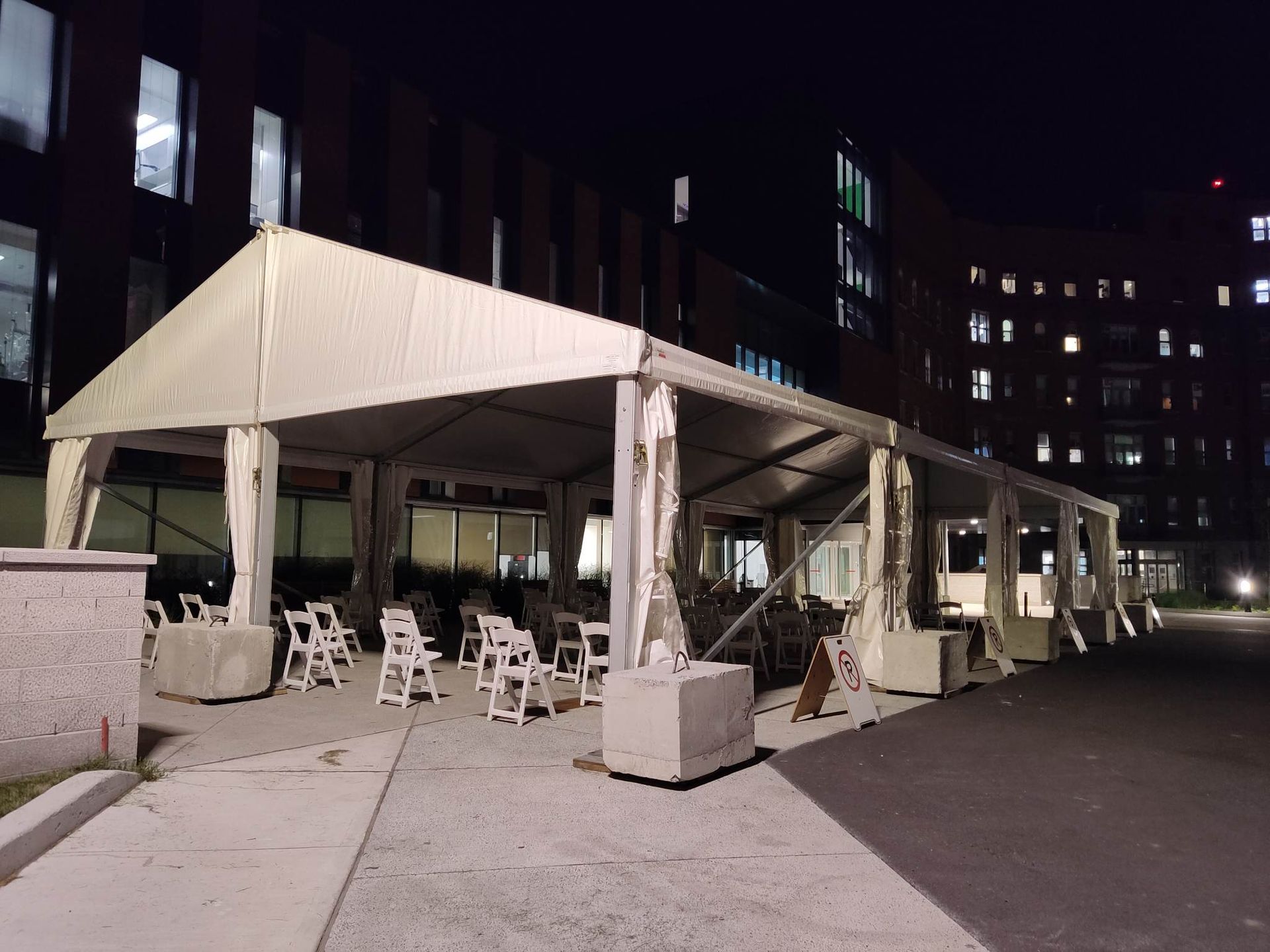 Une grande tente blanche avec des chaises en dessous la nuit