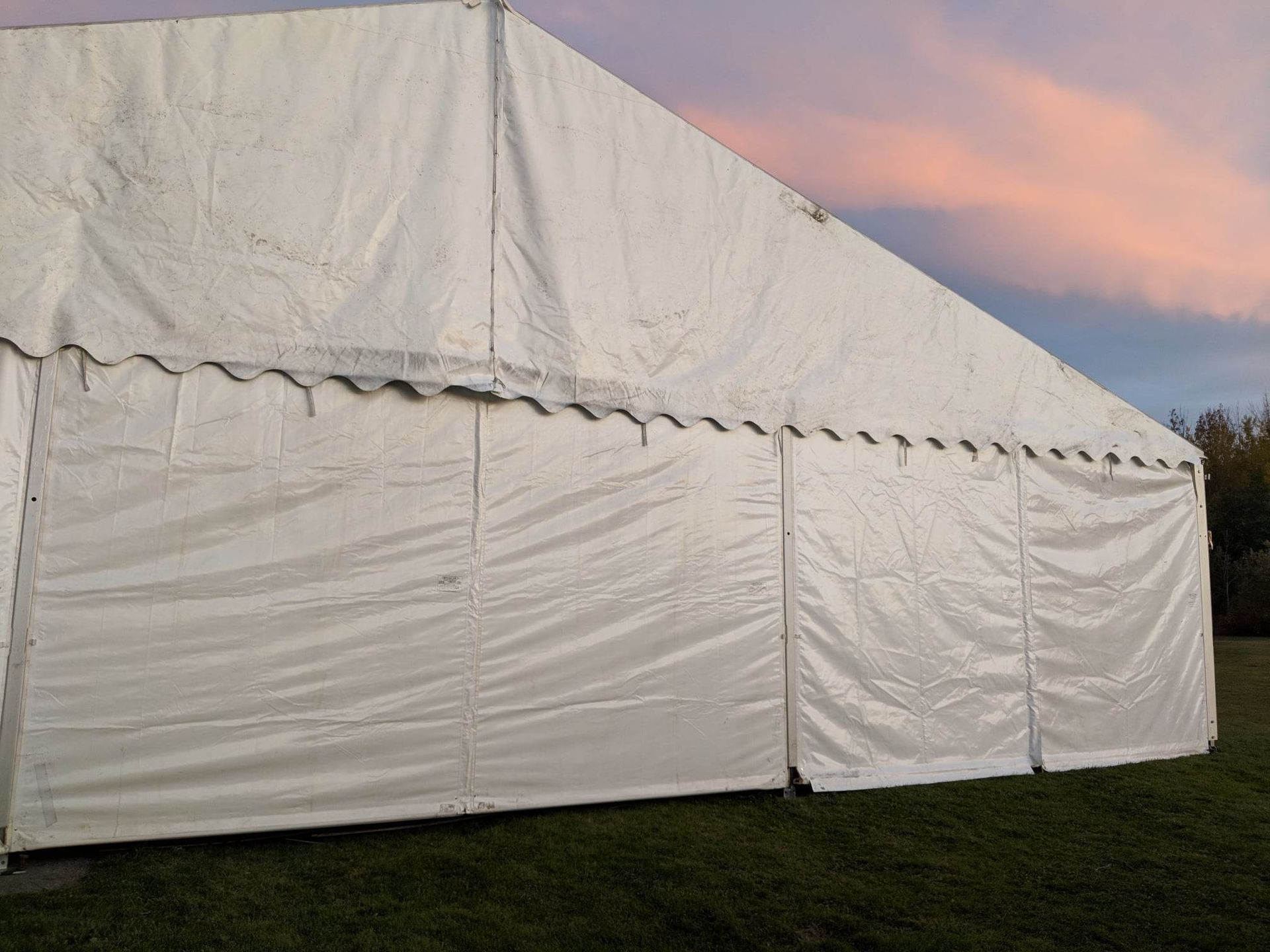 Une grande tente blanche est dressée au milieu d’un champ herbeux.