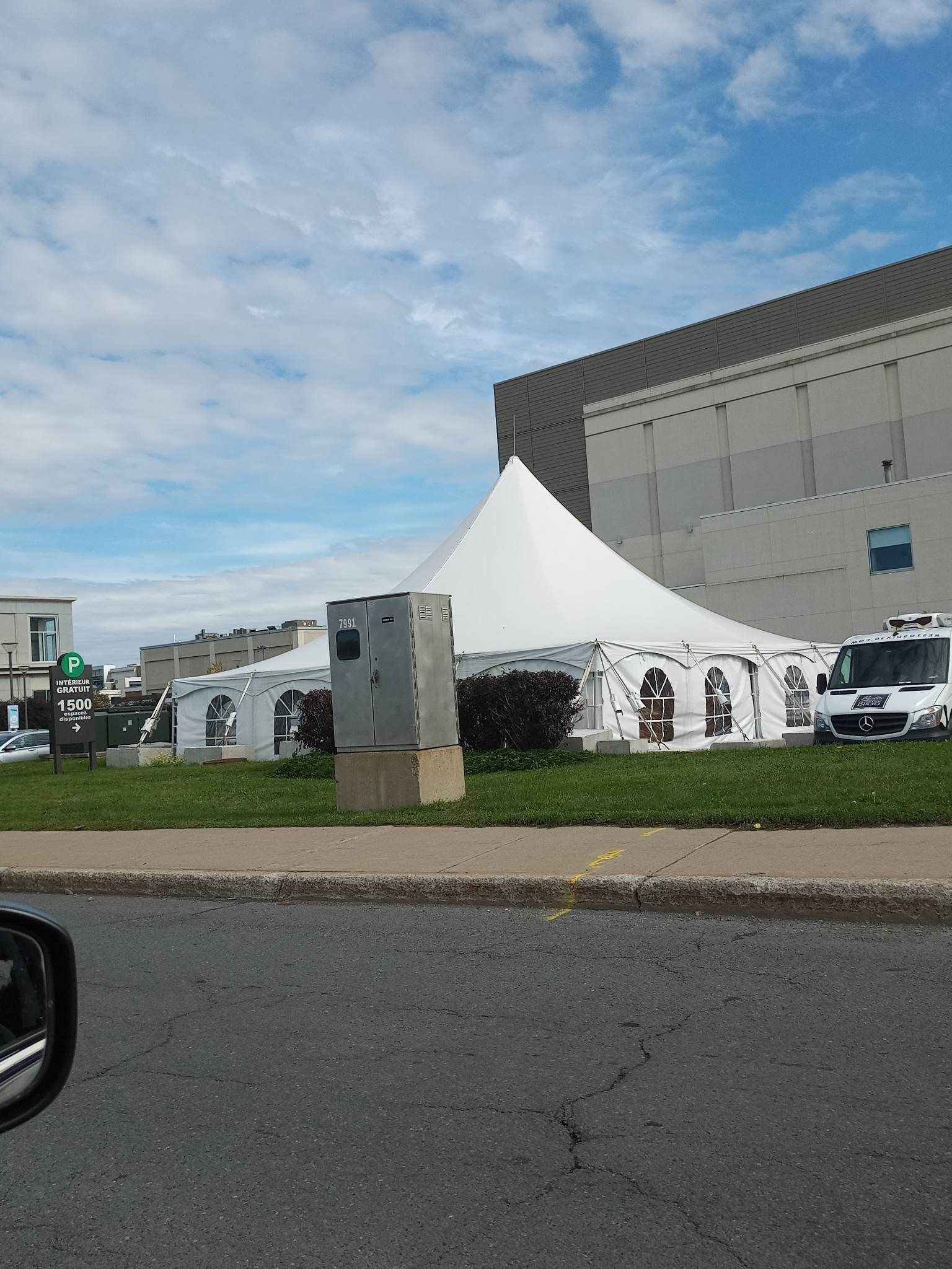 Une tente blanche est installée au bord de la route, devant un immeuble.