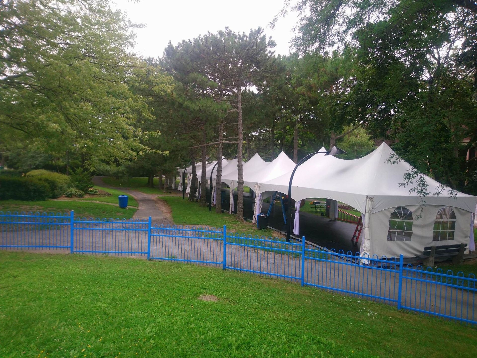 Une rangée de tentes est alignée dans un parc derrière une clôture bleue.