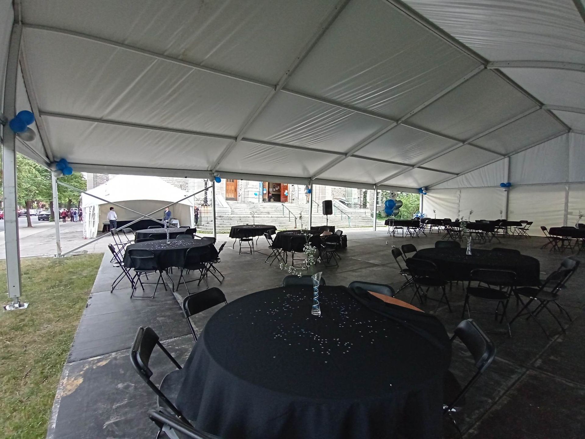 Une grande tente blanche avec des tables et des chaises noires en dessous.