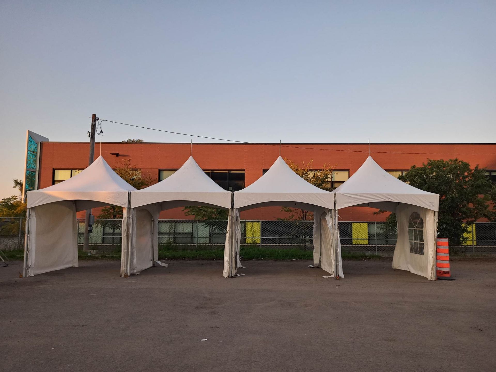 Une rangée de tentes est alignée sur un parking devant un immeuble.