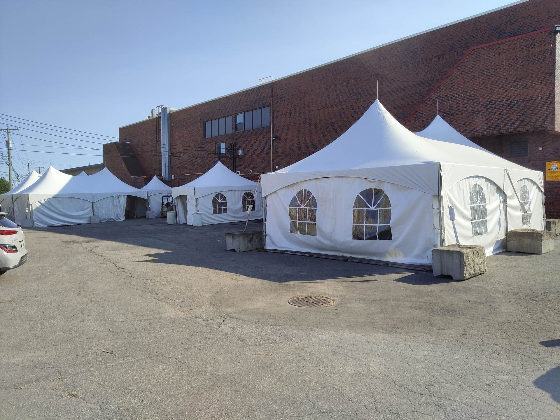 Une rangée de tentes blanches sont alignées devant un bâtiment en brique
