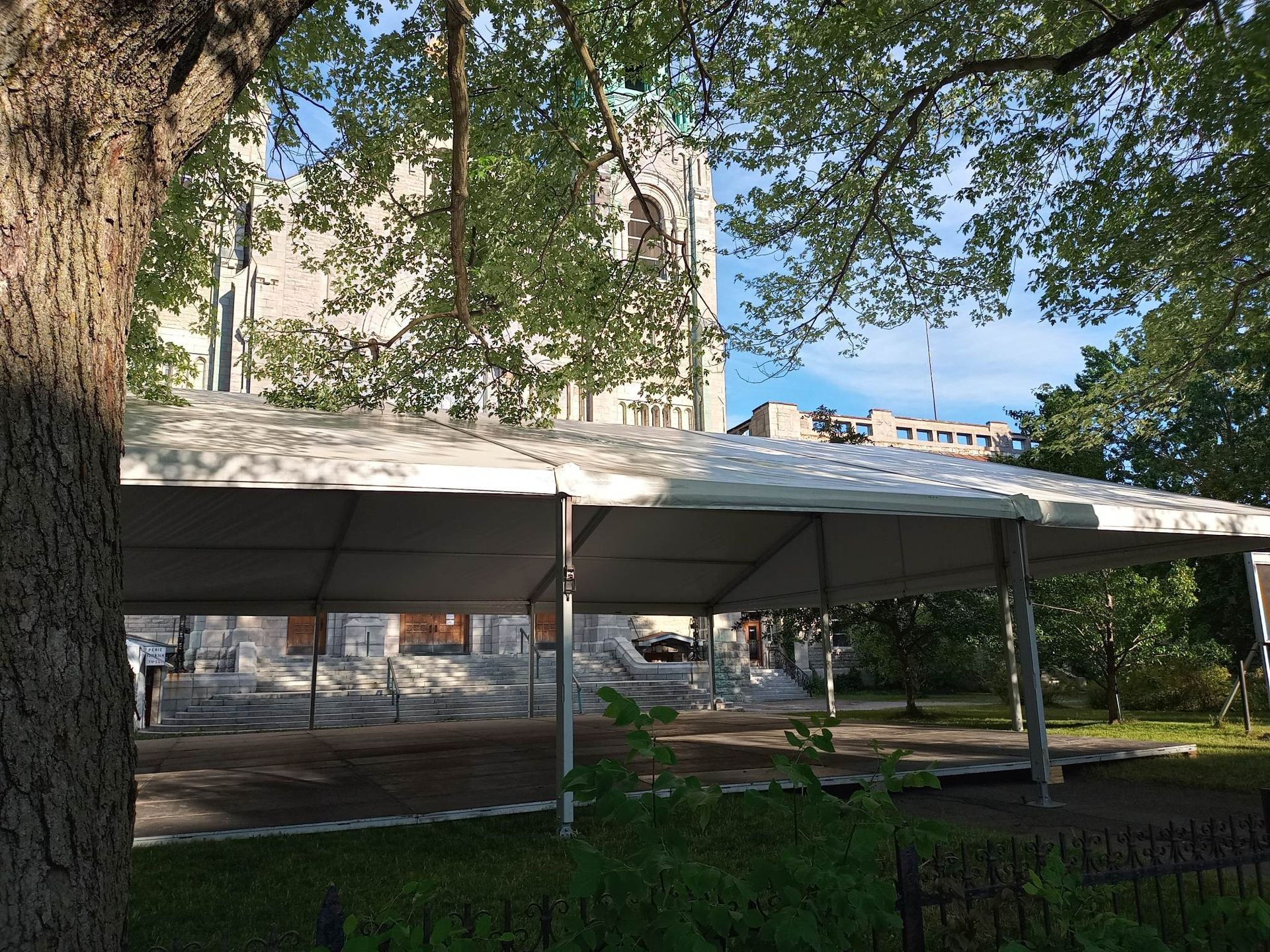 Une grande tente blanche est installée sous un arbre devant un bâtiment.