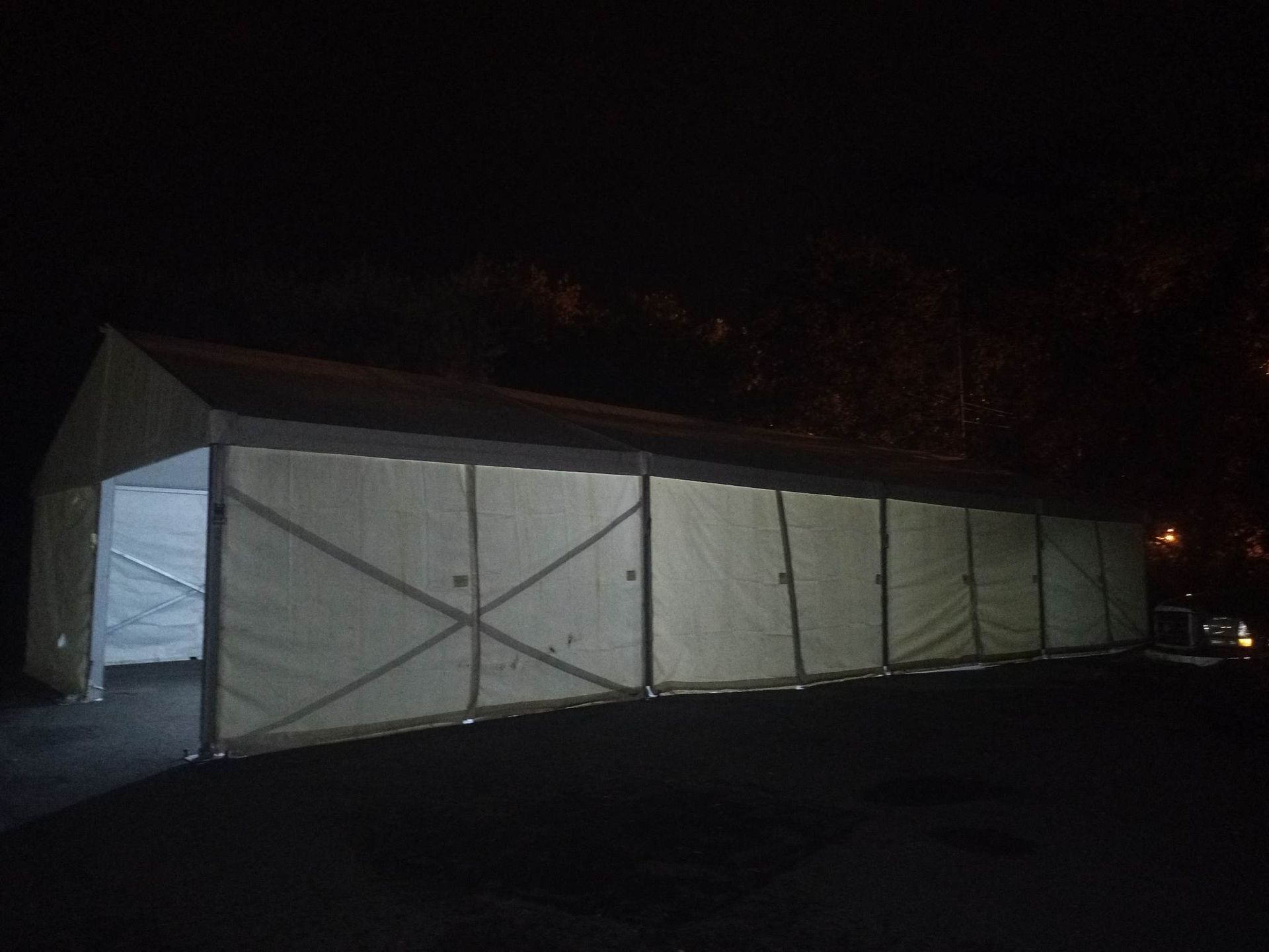 Une grande tente blanche est éclairée la nuit sur un parking.