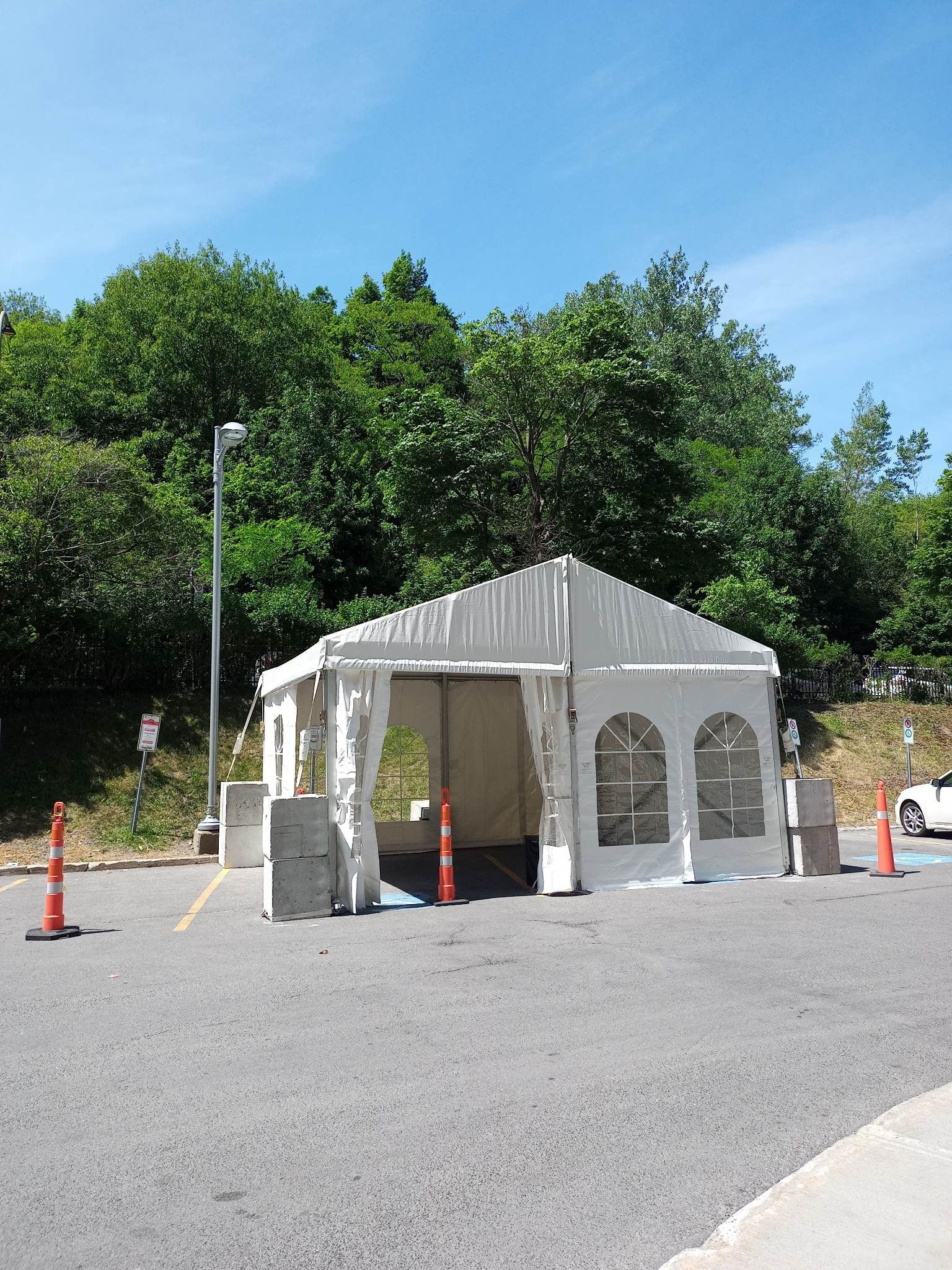 Une tente blanche trône au milieu d’un parking en gravier.