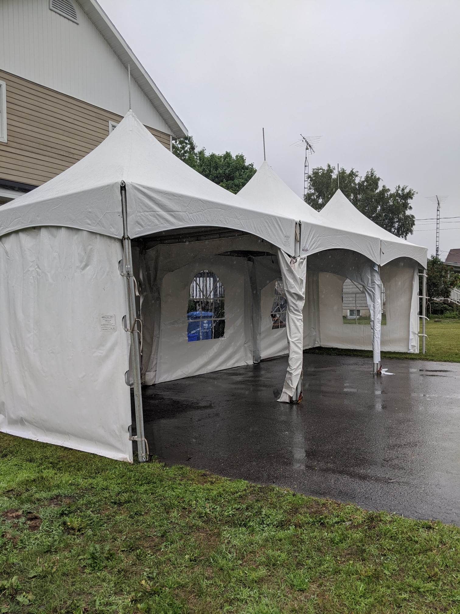 Une rangée de tentes blanches sont posées dans l’herbe devant une maison.