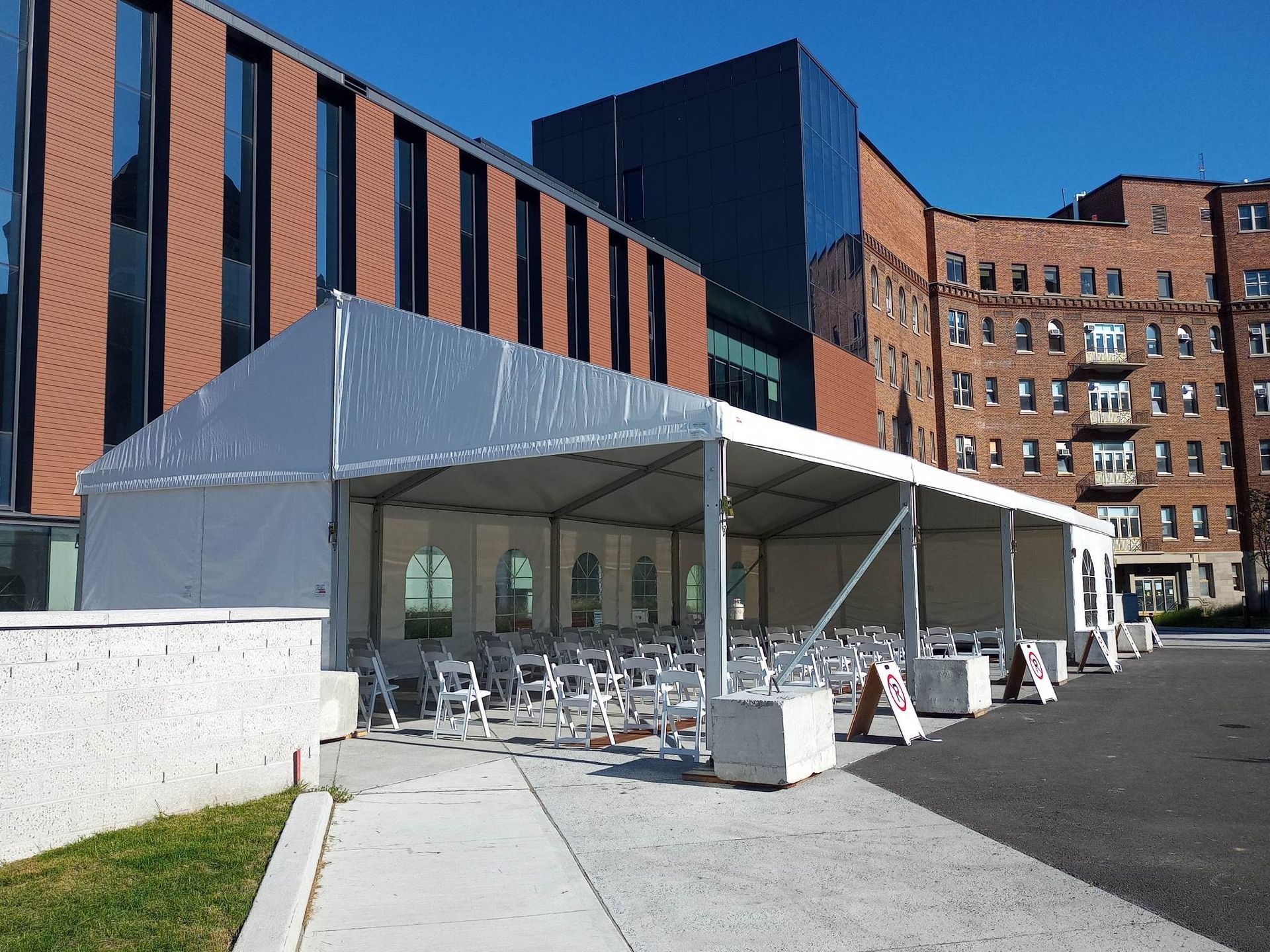 Une grande tente blanche trône devant un grand bâtiment en brique.