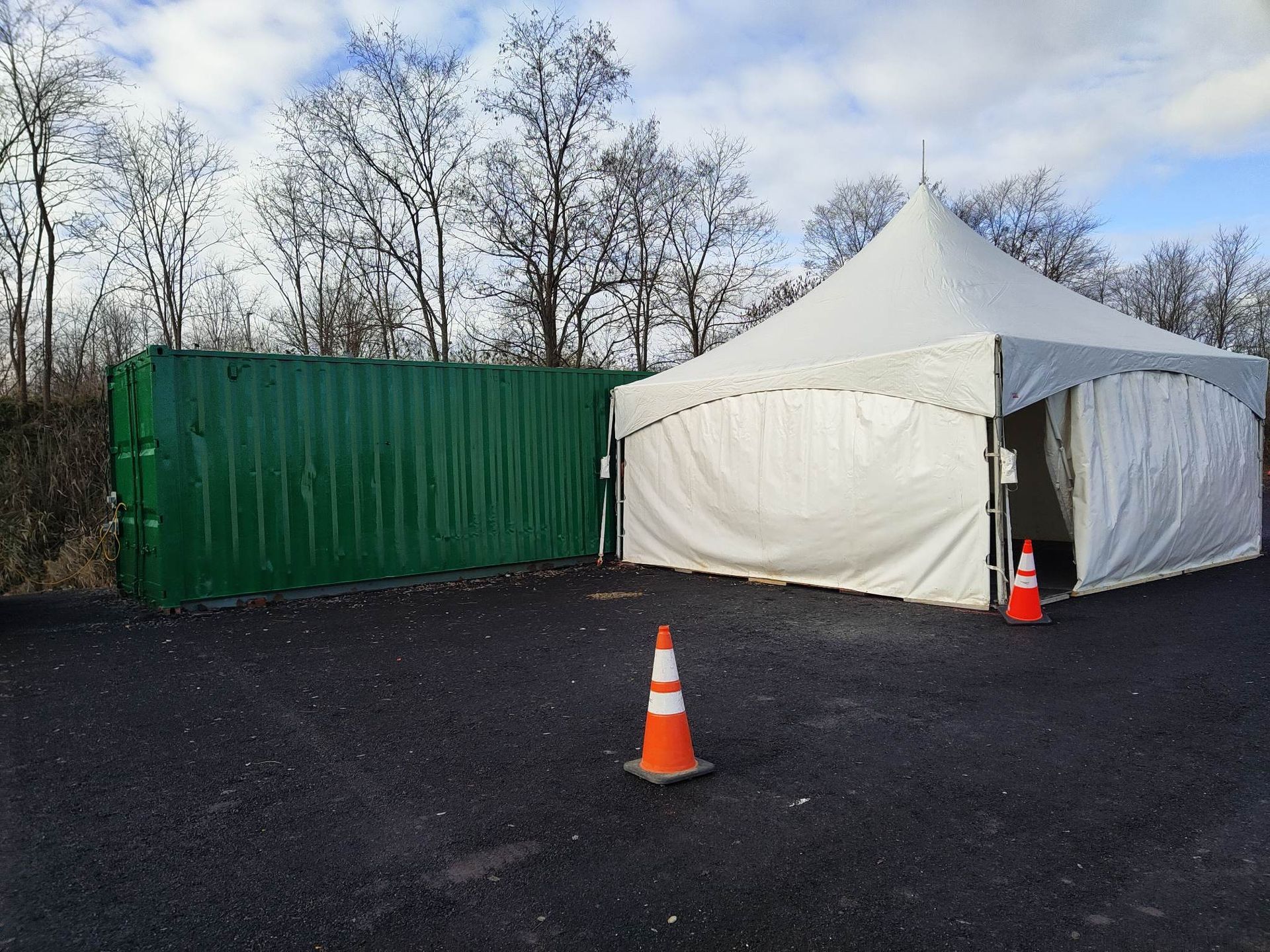 Une tente blanche se trouve à côté d’un conteneur vert dans un parking.