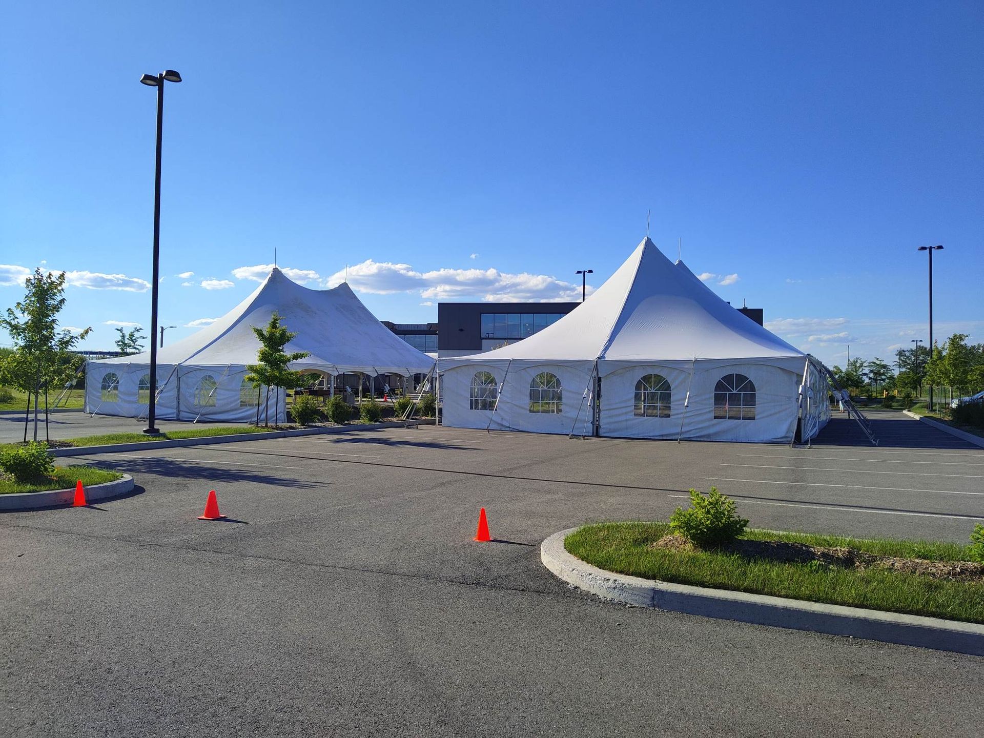 Deux tentes blanches se trouvent sur un parking devant un immeuble.