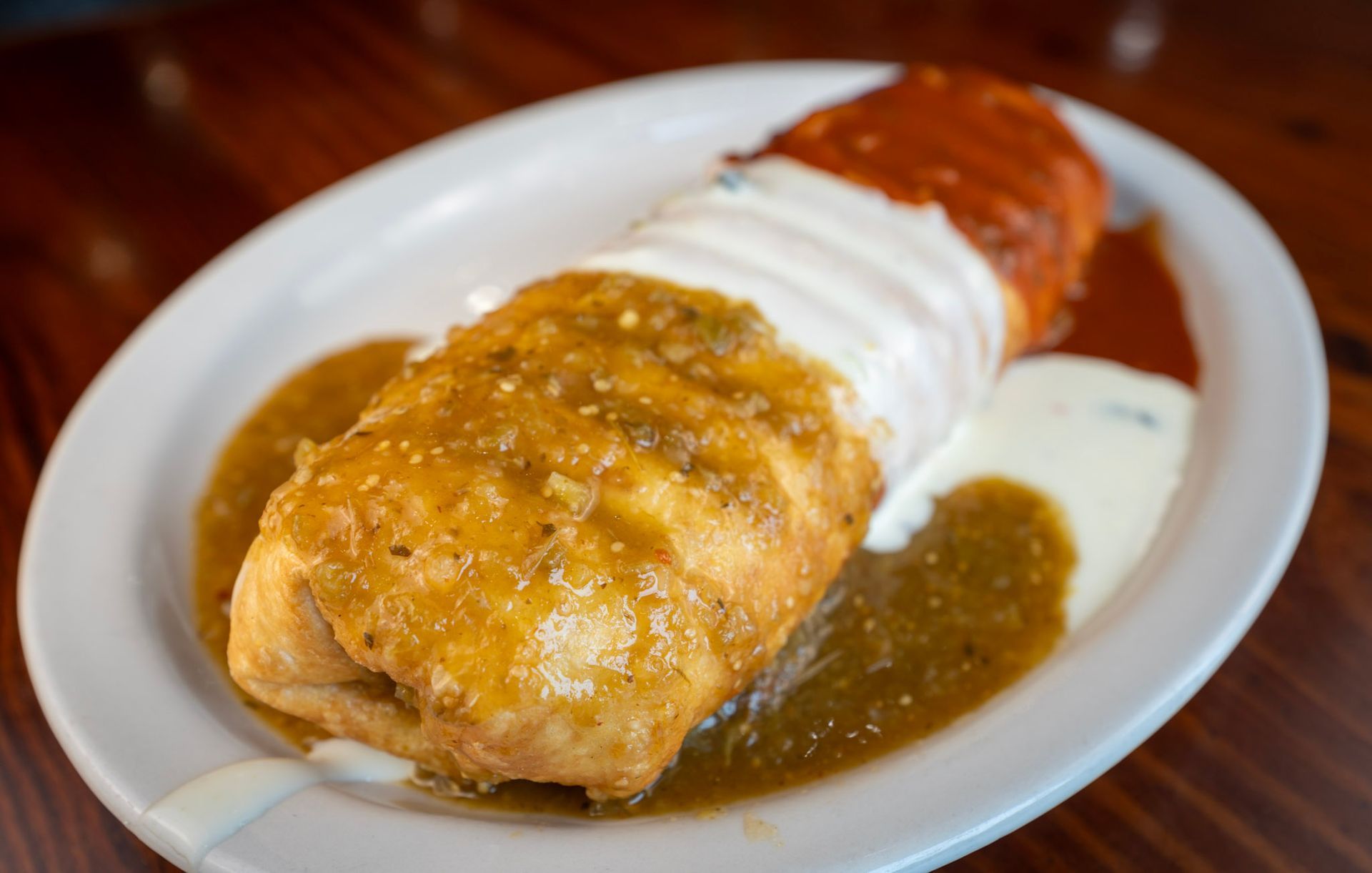 A burrito with sauce and sour cream on a white plate on a table.
