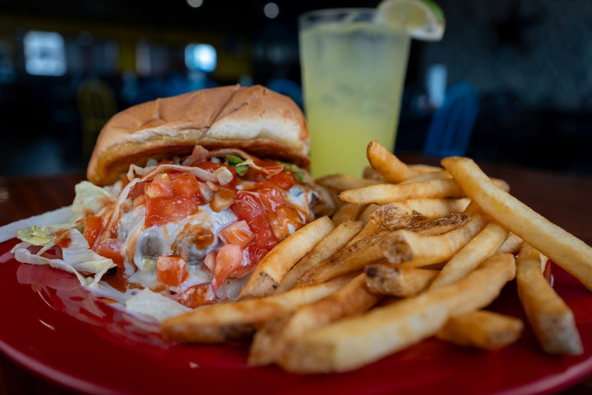 A hamburger and french fries on a red plate with a drink in the background.