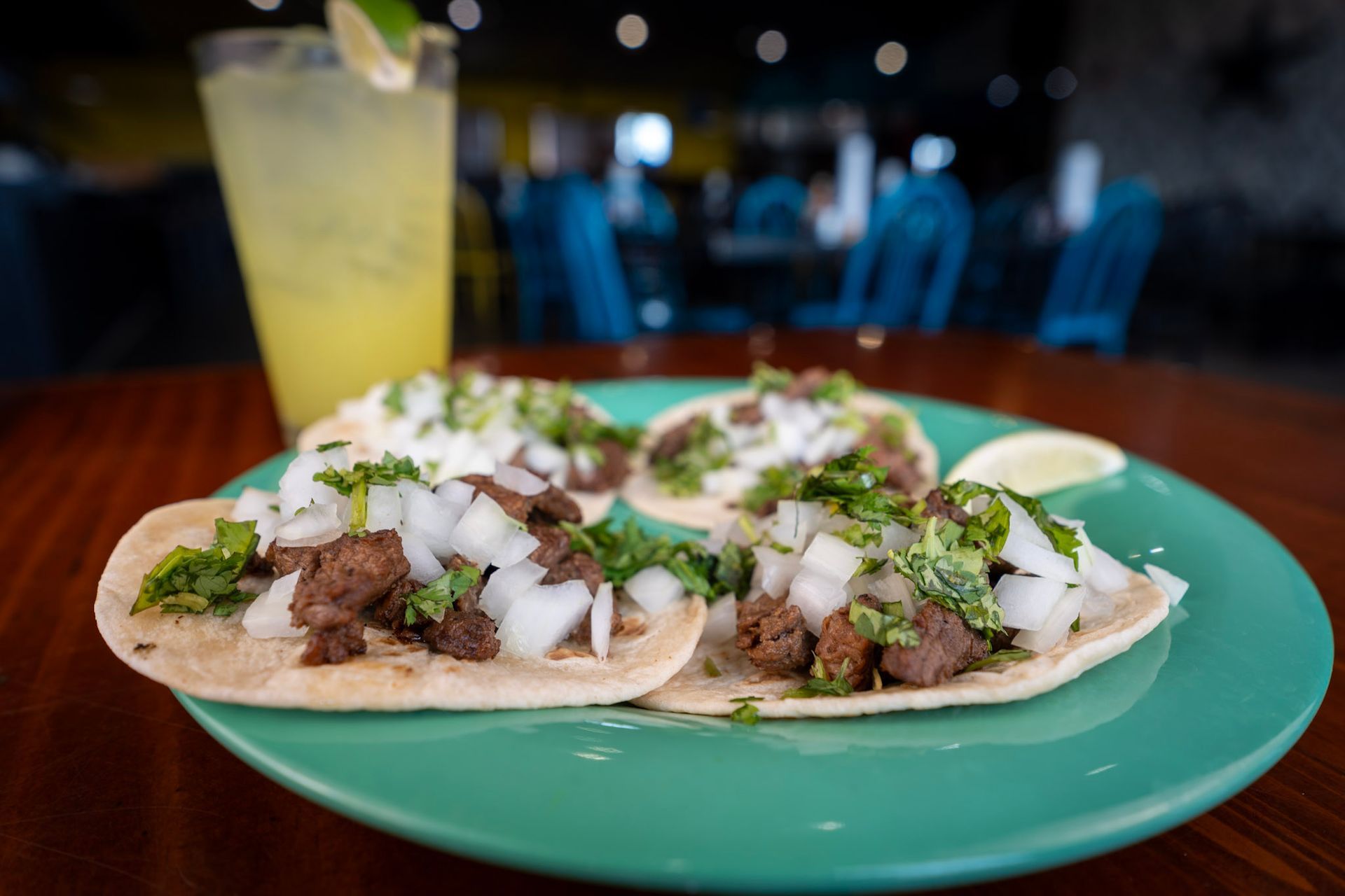A close up of a plate of tacos on a table with a drink in the background.