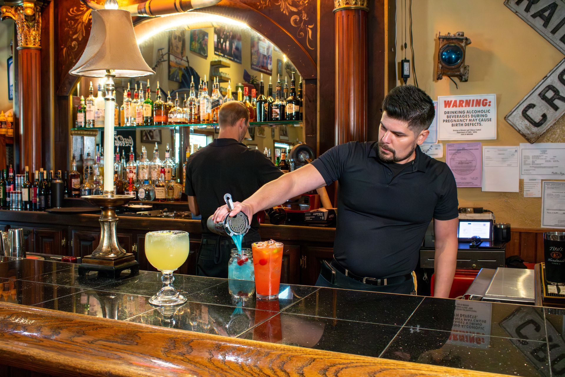 A man is pouring a drink into a glass at a bar.