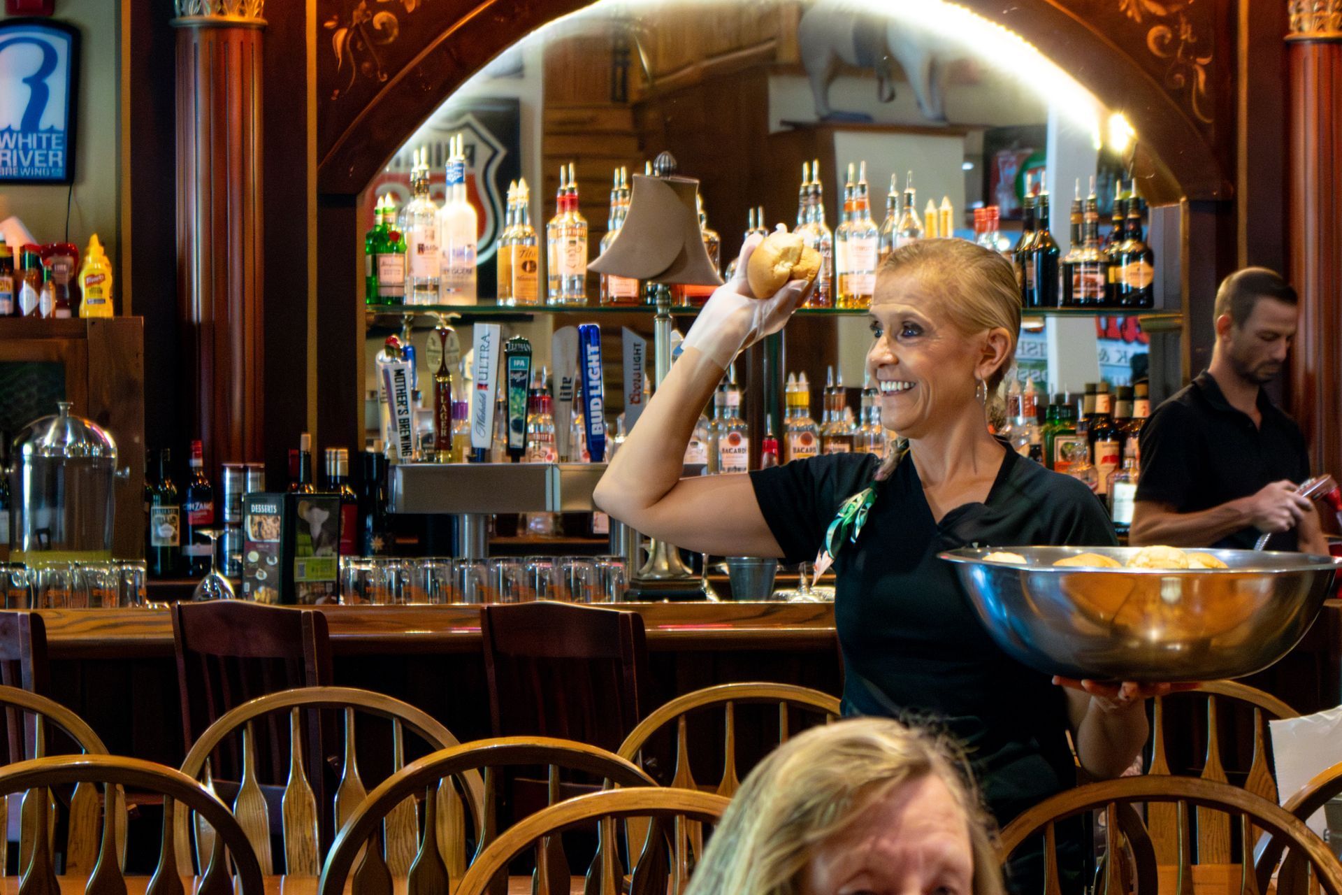 A woman is holding a bowl of food in front of a bar.