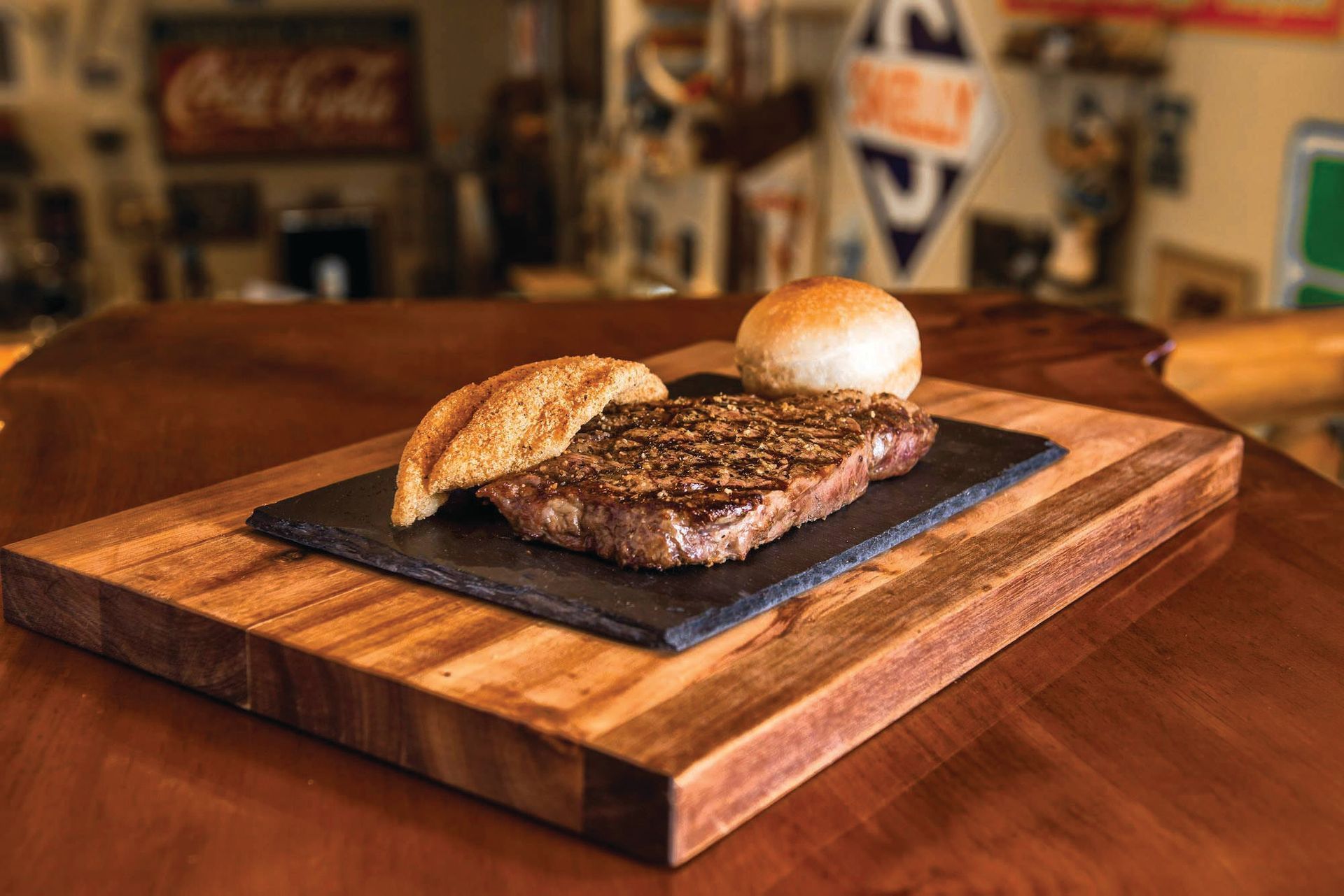 A steak and a bun on a wooden cutting board on a table.