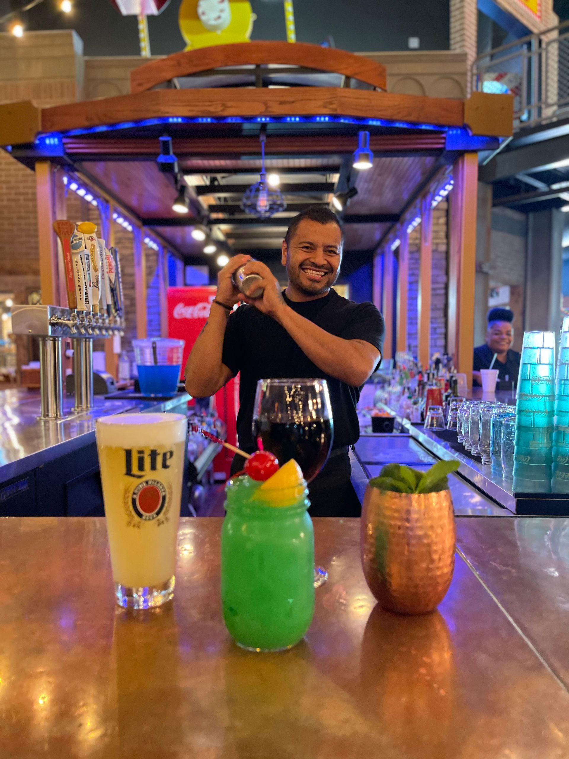 A man is standing behind a bar making a drink.