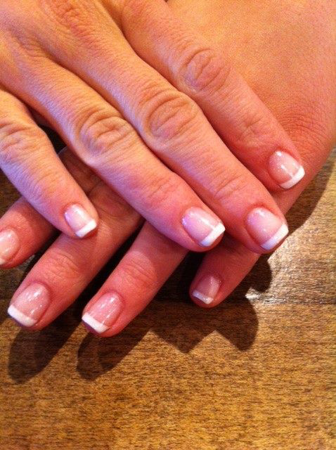 Hands with French manicure resting on a wooden table.