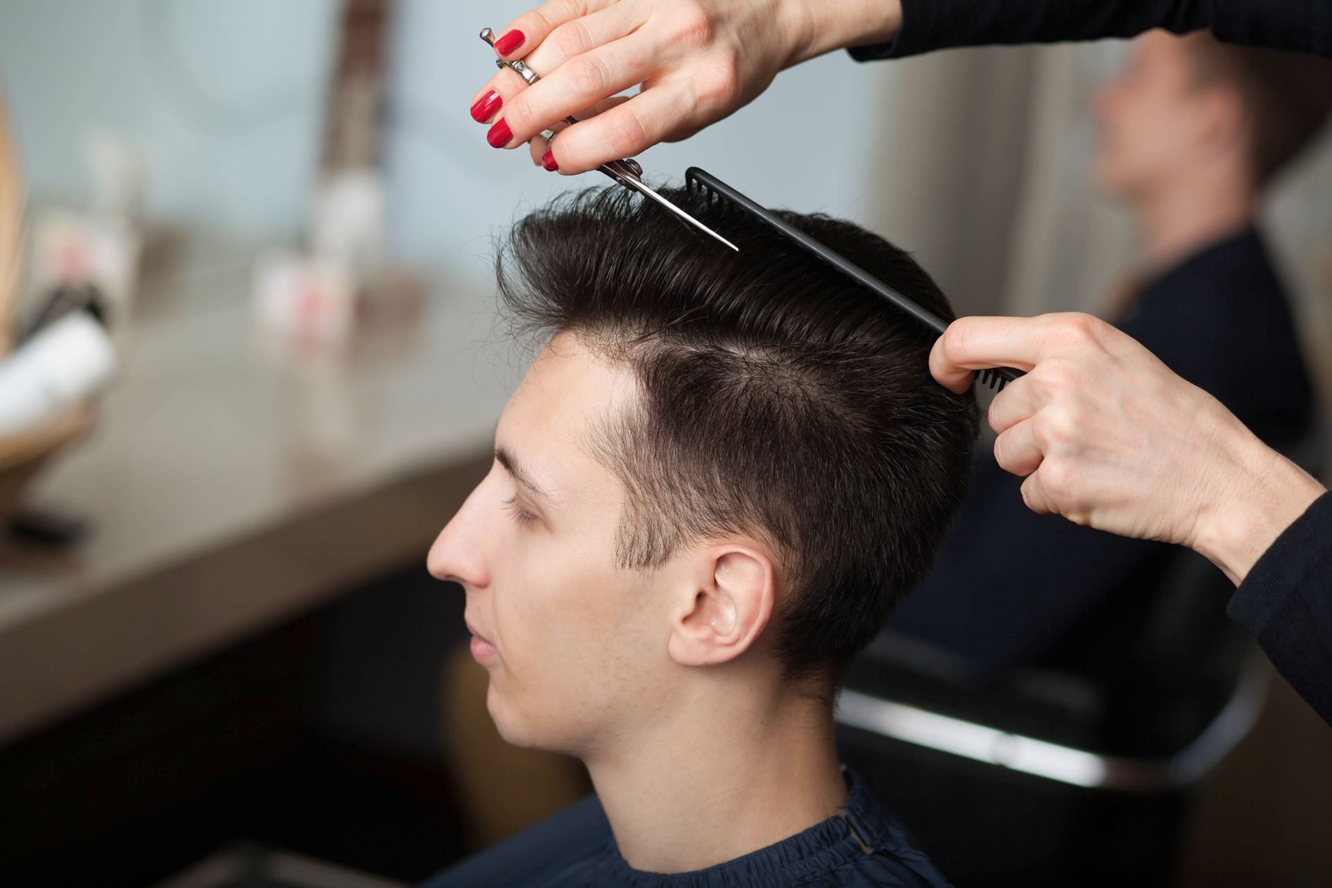 Hairdresser cutting a man’s hair with scissors and comb in a salon