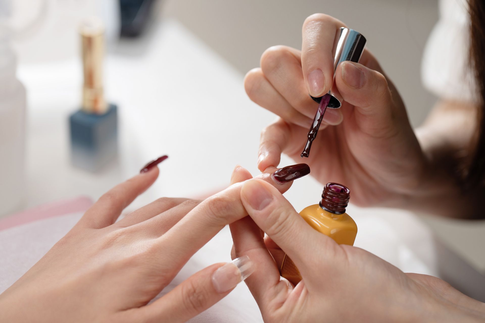 Manicured hands applying nail polish to another person's fingernails in a salon