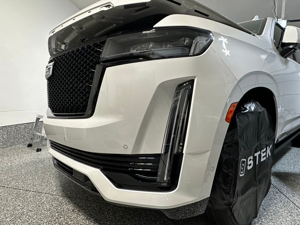 White Cadillac SUV with black grill, front bumper, and covered tire in a garage.